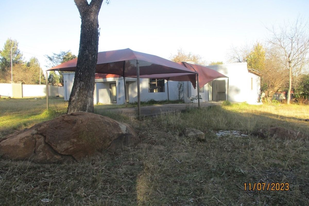 Rear view of the residential property featuring a concrete patio area with a shade sail, set within a large, overgrown garden plot.