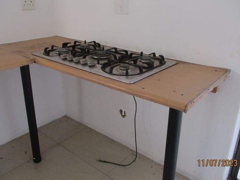 A basic kitchen area featuring a built-in gas hob set into a simple laminate countertop with metal support legs and tiled flooring.