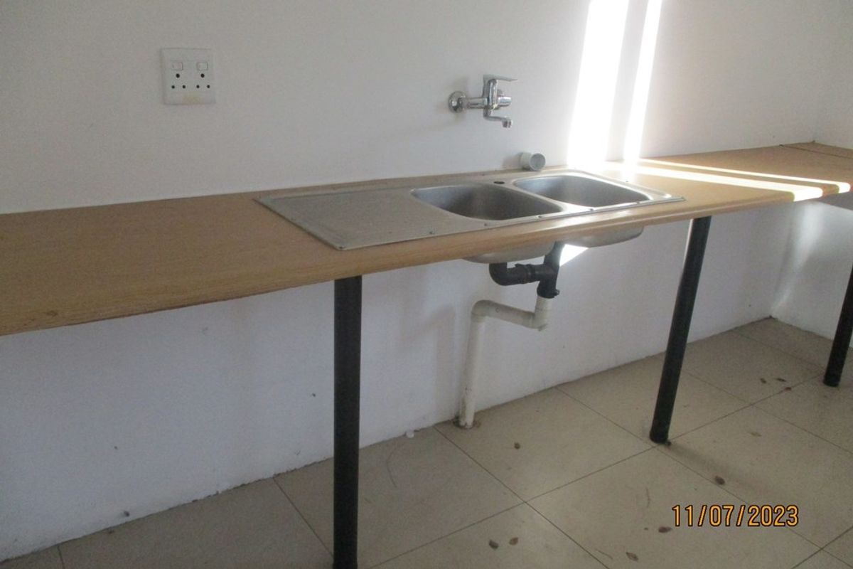 A basic kitchen area featuring a double bowl stainless steel sink, laminate countertop, and tiled flooring, currently lacking cabinetry.