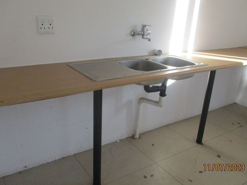 A basic kitchen area featuring a double bowl stainless steel sink, laminate countertop, and tiled flooring, currently lacking cabinetry.