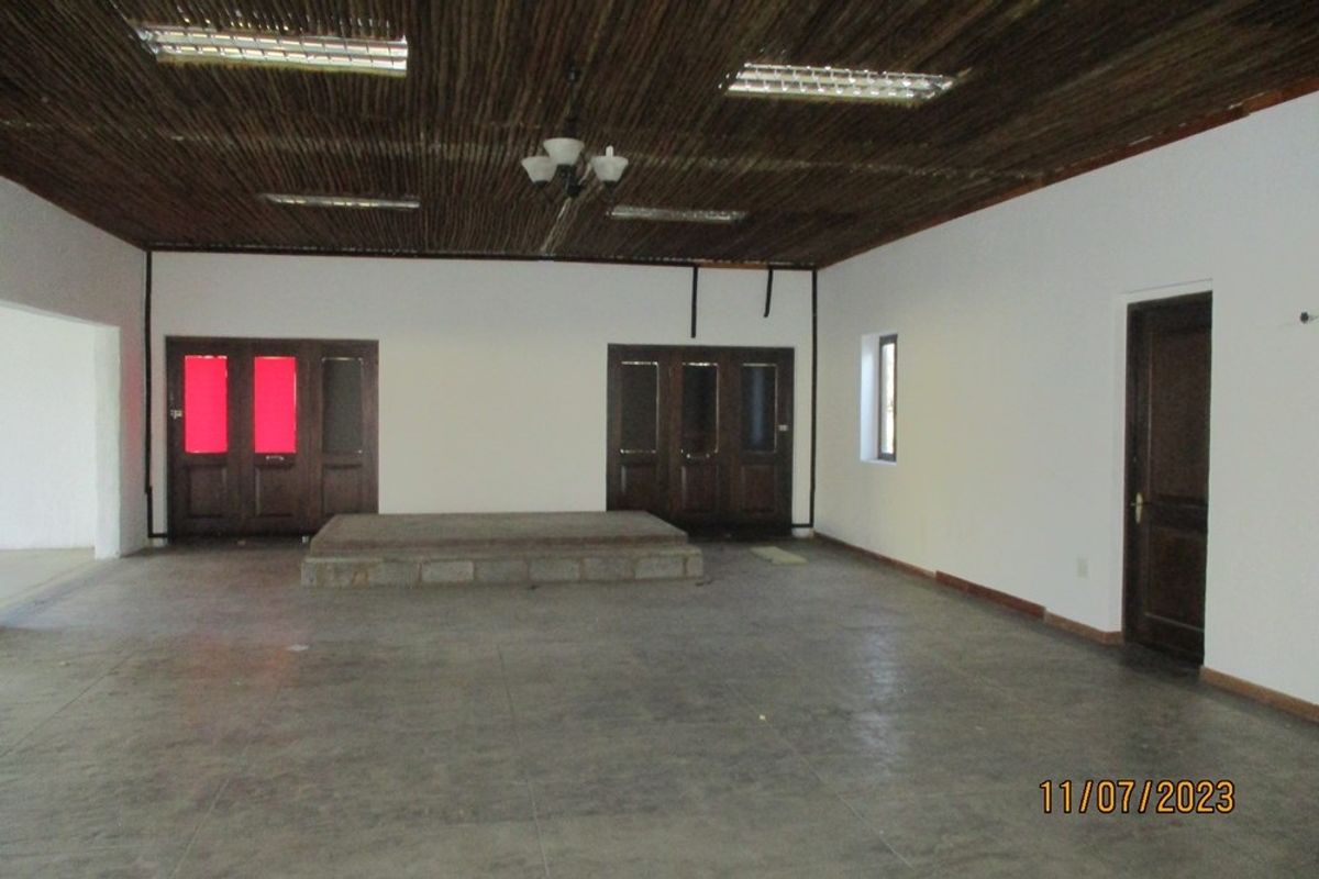 A spacious, vacant interior room featuring a raised concrete platform, unique thatch ceiling, and tiled flooring, suitable for various functional uses.