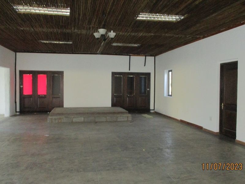 A spacious, vacant interior room featuring a raised concrete platform, unique thatch ceiling, and tiled flooring, suitable for various functional uses.
