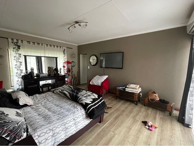 Spacious bedroom featuring wood-look laminate flooring, a wall-mounted air conditioning unit, and large windows allowing for natural light.