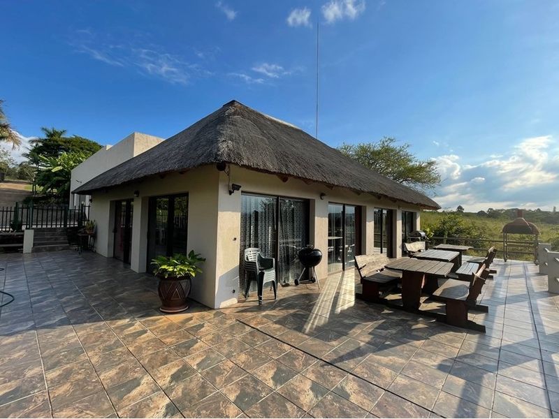 Spacious outdoor patio area featuring tiled flooring and a traditional thatched roof, overlooking the surrounding landscape.