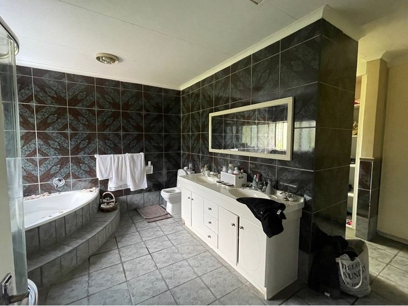 Spacious bathroom featuring a corner soaking tub, dual vanity unit with integrated sinks, and dark decorative wall tiling.
