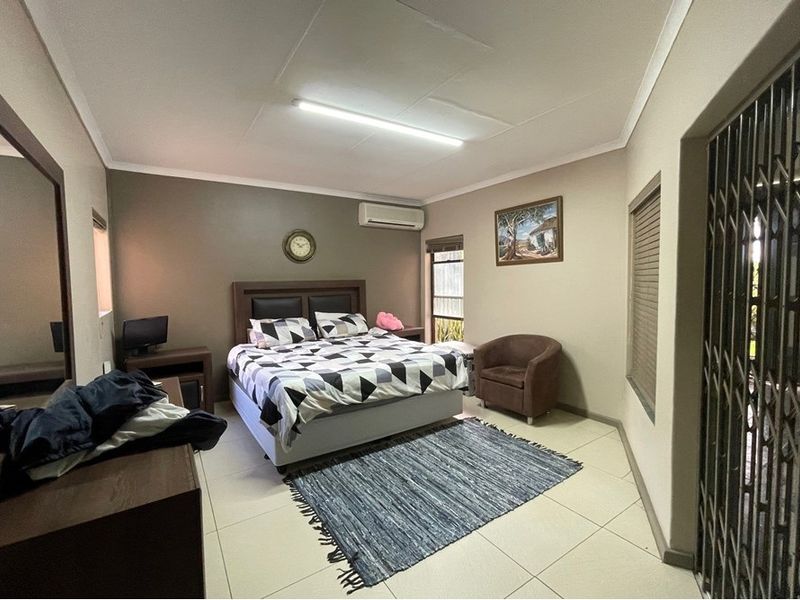 A spacious bedroom featuring tiled flooring, a wall-mounted air conditioning unit, and a security gate at the entrance.