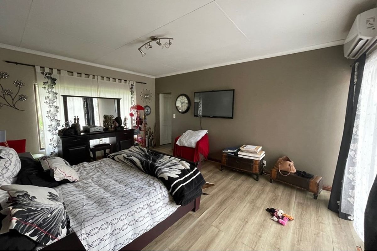 Spacious bedroom featuring wood-look laminate flooring, a wall-mounted air conditioning unit, and large windows allowing for natural light.