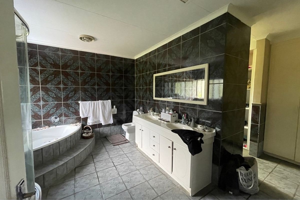 Spacious bathroom featuring a corner soaking tub, dual vanity unit with integrated sinks, and dark decorative wall tiling.