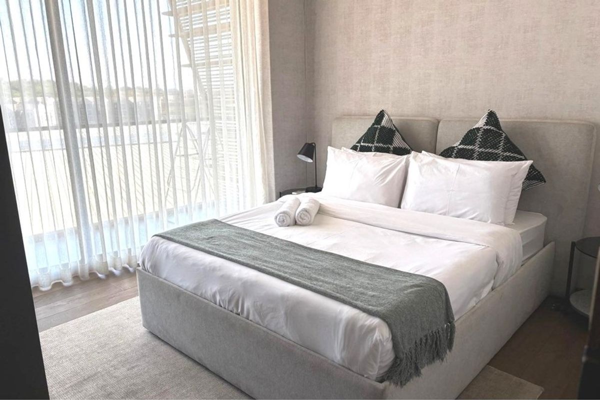A well-maintained bedroom featuring neutral wall finishes, timber flooring, and large sliding glass doors providing access to an outdoor balcony area.