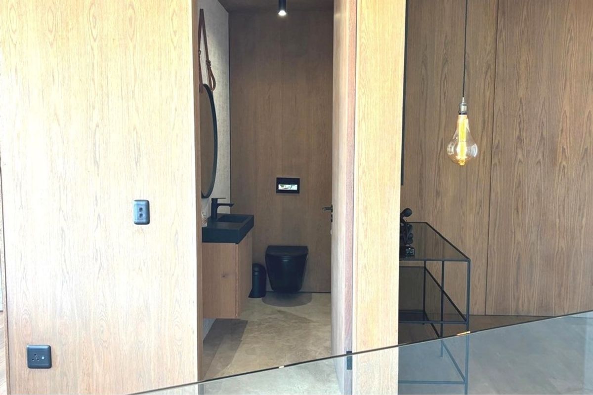 A modern guest bathroom featuring wood-paneled walls, a floating vanity with a black basin, and a wall-mounted toilet with a sleek black finish.
