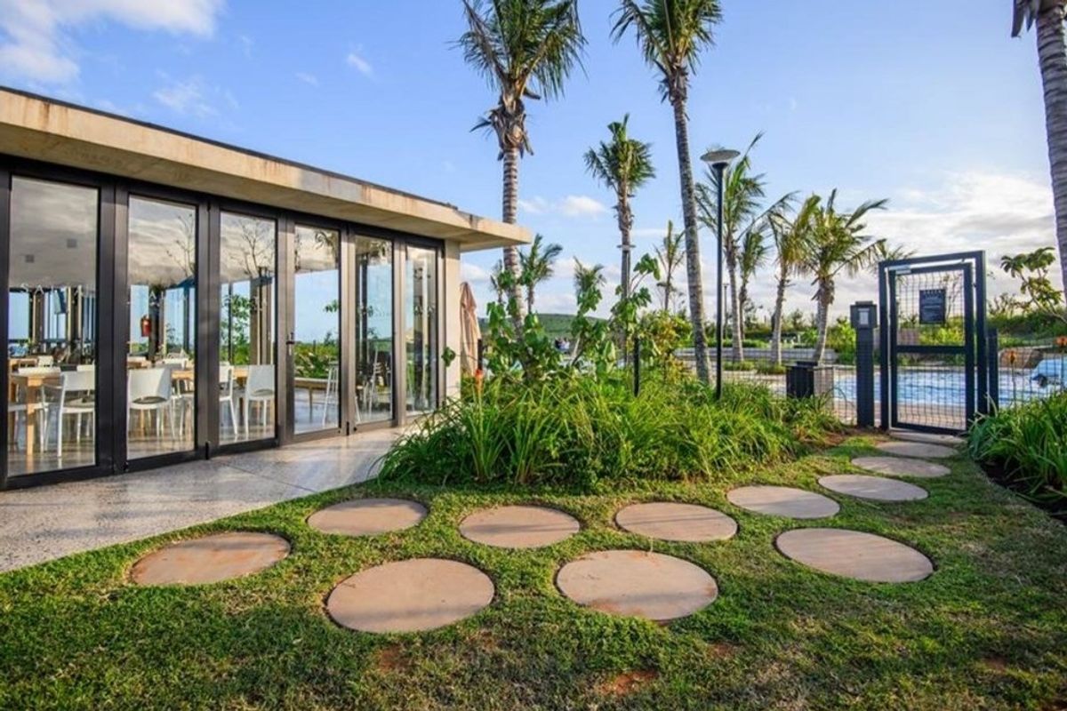 A well-maintained outdoor area featuring a modern building with floor-to-ceiling glass doors, landscaped garden with circular pavers, and access to a pool area.