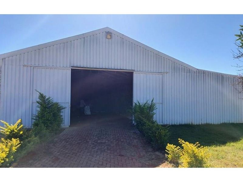 A large farm shed or barn featuring corrugated metal cladding, sliding doors, and a paved entrance path.