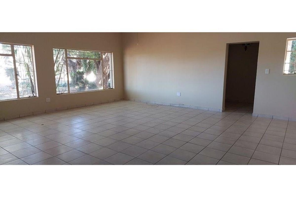 A spacious, empty living area featuring neutral tiled flooring and large windows, providing a blank canvas for interior design and renovation.