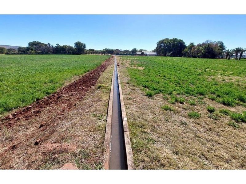 An expansive agricultural field featuring a central concrete irrigation canal running through the property.