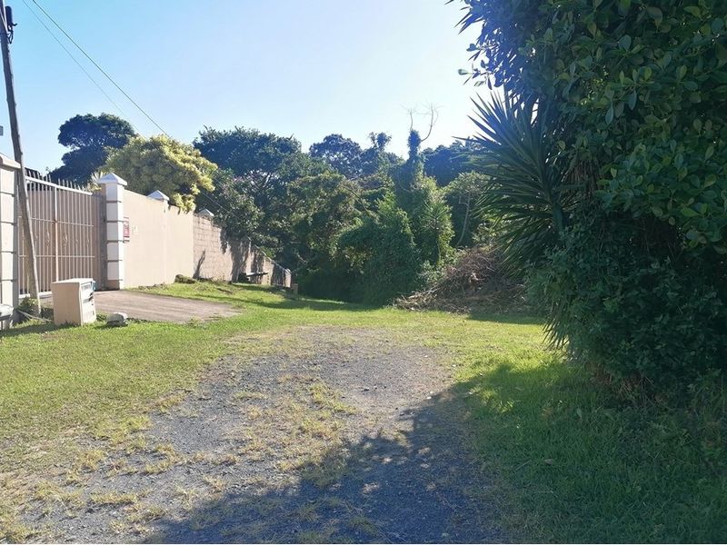 A view of the vacant residential land featuring a boundary wall, metal gate, and an existing driveway entrance.