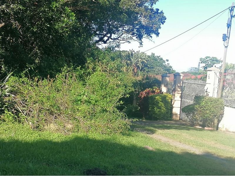 A view of the property entrance featuring a metal gate, masonry pillars, and established garden landscaping.