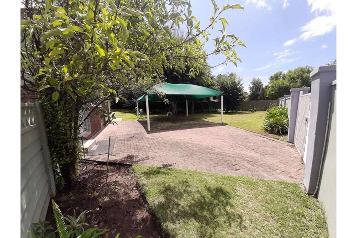 A spacious rear garden featuring a paved patio area, a green shade sail structure, and established lawn and perimeter fencing.