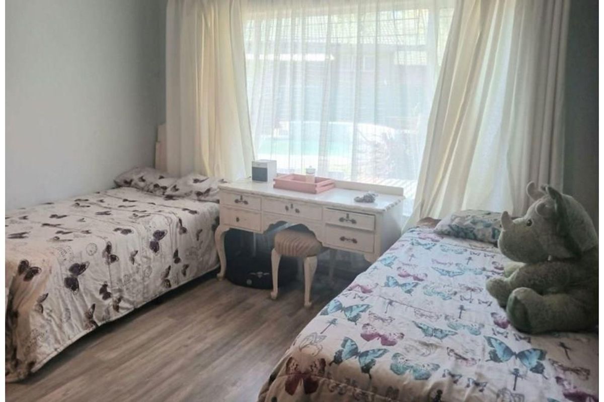 A bedroom featuring light-toned wood-look flooring and a large window with sheer curtains, providing natural light and a view of the outdoor area.