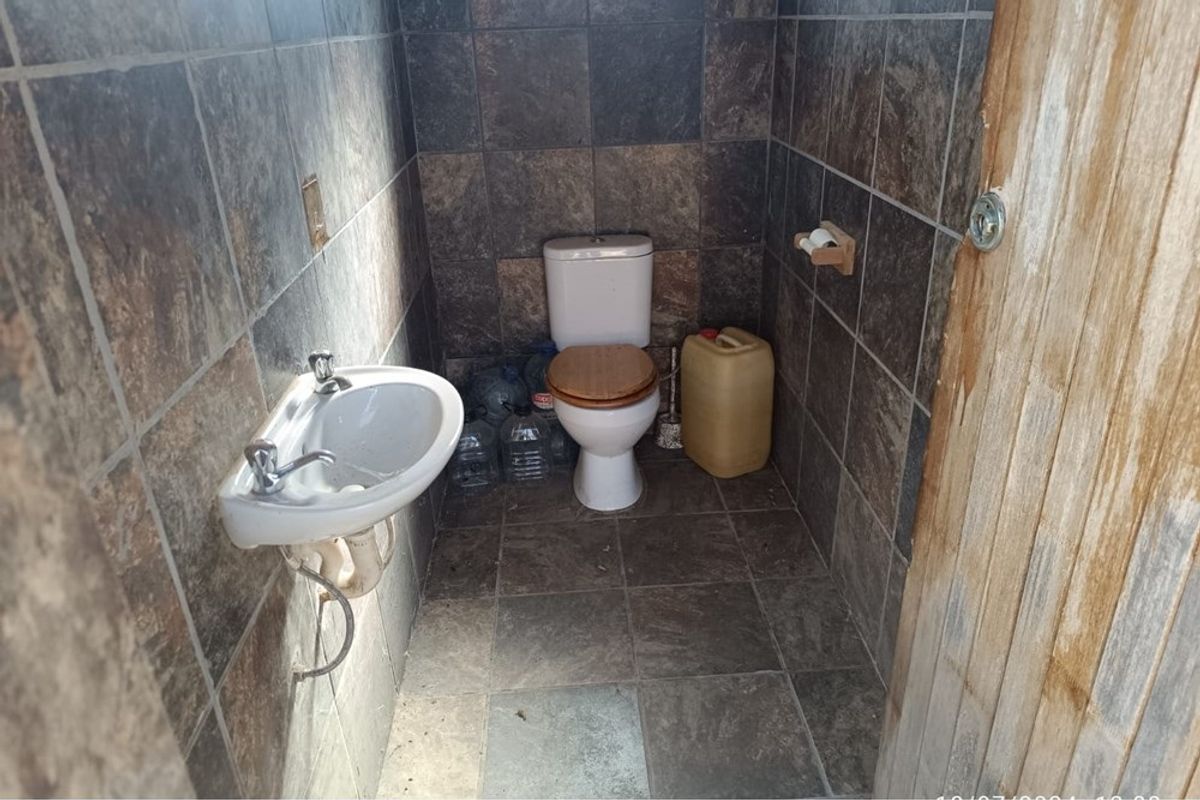 A small bathroom featuring dark stone-look wall and floor tiles, equipped with a standard toilet and a wall-mounted basin.