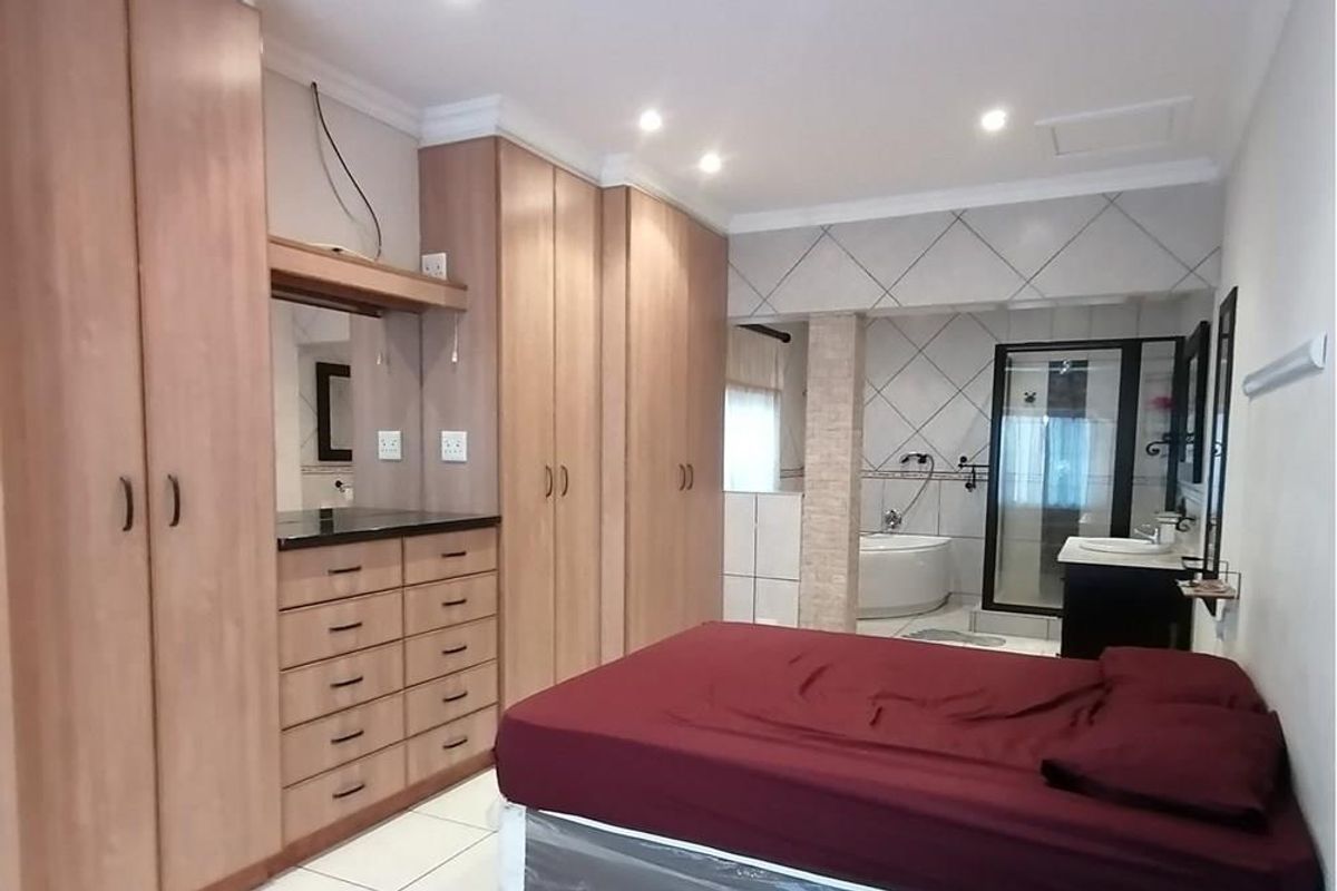 Spacious bedroom featuring extensive built-in wooden cabinetry and an open-plan en-suite bathroom with a corner bathtub and glass shower enclosure.