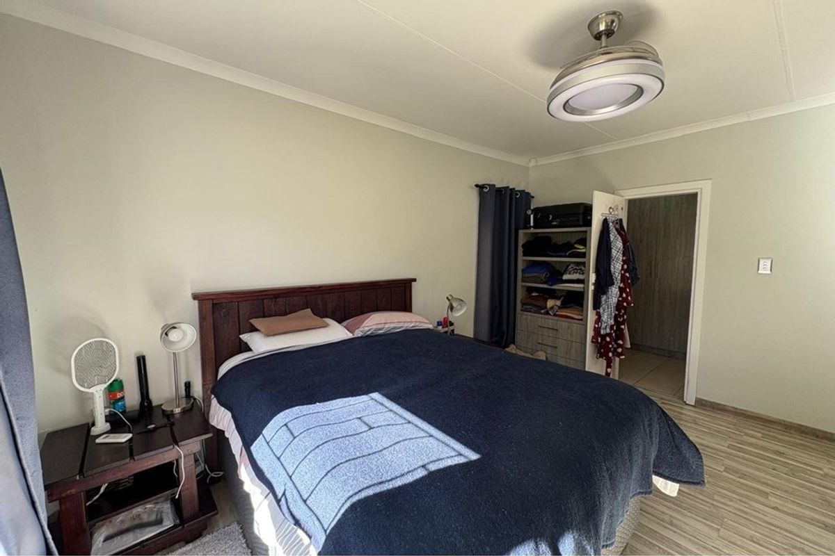 A well-lit bedroom featuring light-toned laminate flooring, neutral wall finishes, and a modern ceiling light fixture.