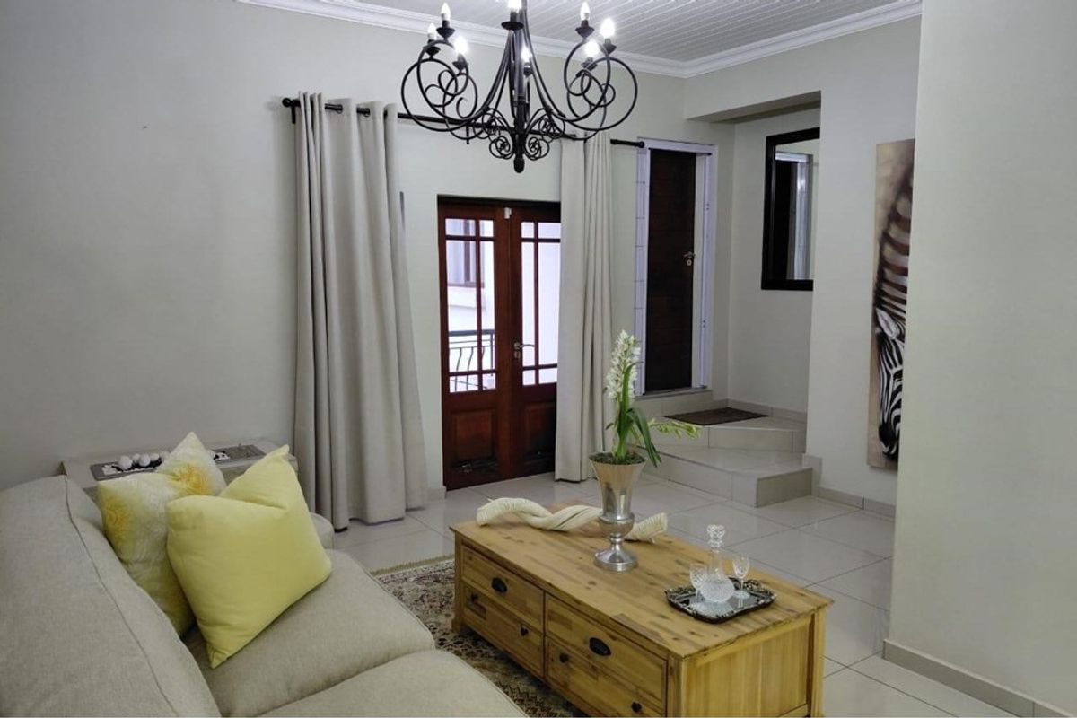 A well-maintained living room featuring tiled flooring, crown molding, and a classic chandelier, providing a bright and welcoming atmosphere.