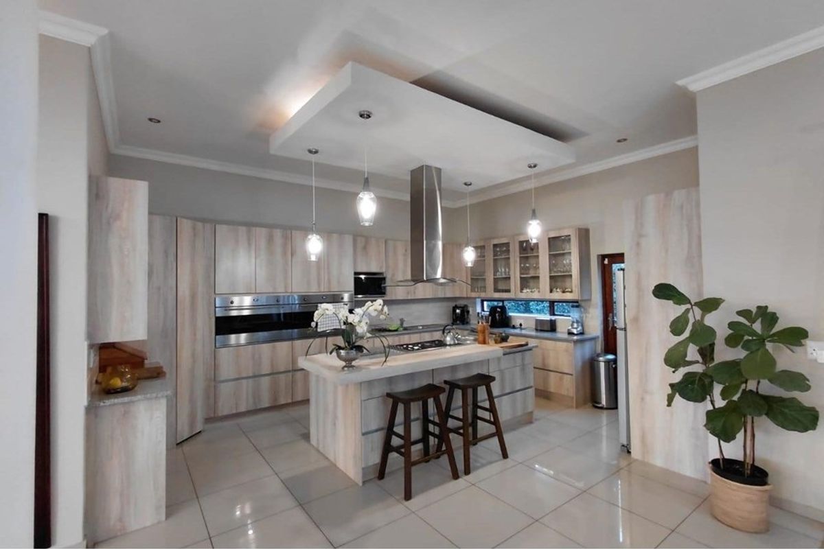 Modern kitchen featuring light wood cabinetry, a central island with a built-in cooktop, stainless steel appliances, and a suspended bulkhead with pendant lighting.