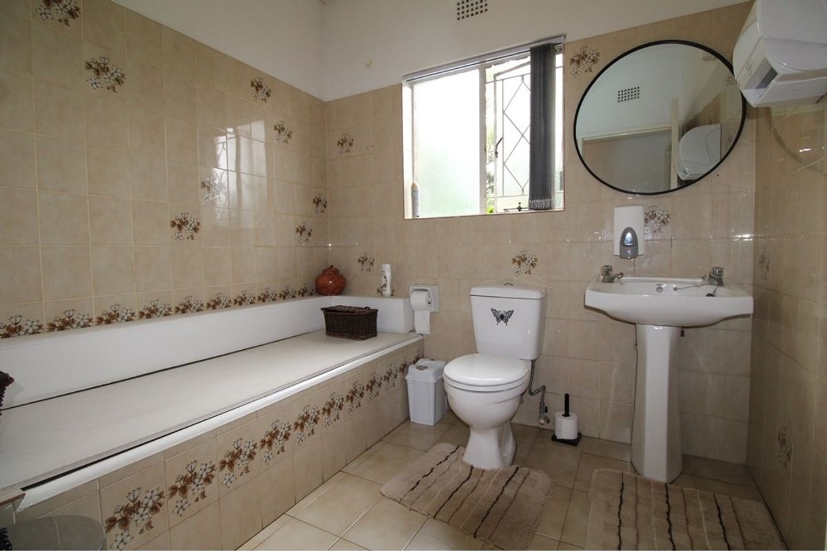 A dated bathroom featuring a built-in bathtub, pedestal sink, and toilet with original floral-patterned wall tiles and ceramic floor tiling.