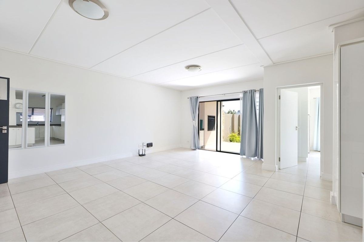 A bright, spacious, and empty living area featuring neutral tiled flooring, clean white walls, and a sliding glass door leading to an outdoor space.