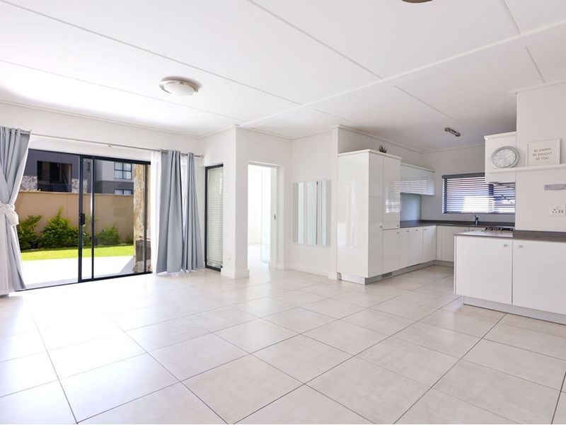 Bright open-plan living and kitchen area featuring neutral tiled flooring, modern white cabinetry, and direct access to an outdoor patio space.
