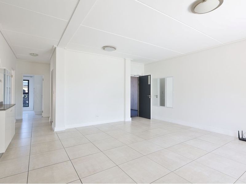 A bright, open-plan living and kitchen area featuring neutral tiled flooring, clean white walls, and functional built-in cabinetry.