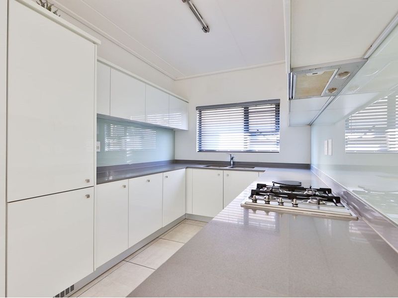A clean, modern kitchen featuring white cabinetry, stone countertops, a gas hob, and a glass splashback, offering a functional and bright workspace.
