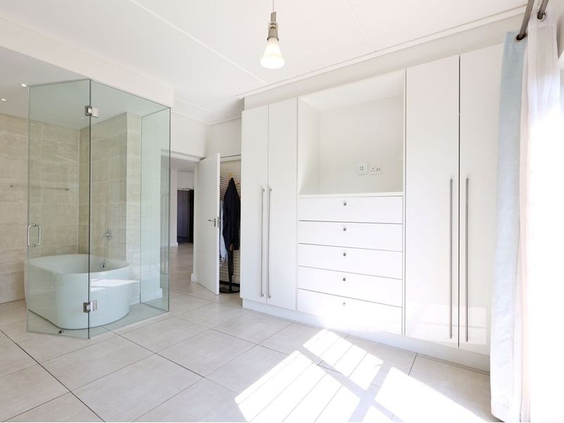 Spacious bedroom featuring a modern glass-enclosed en-suite bathroom with a freestanding tub and extensive built-in wardrobe storage.