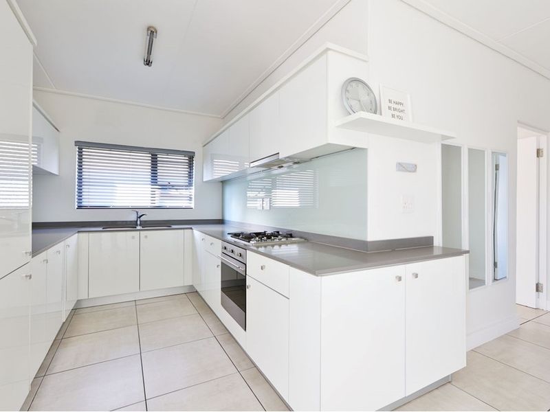 Modern kitchen featuring white gloss cabinetry, stone countertops, a gas hob, integrated oven, and neutral tiled flooring in a clean, minimalist layout.