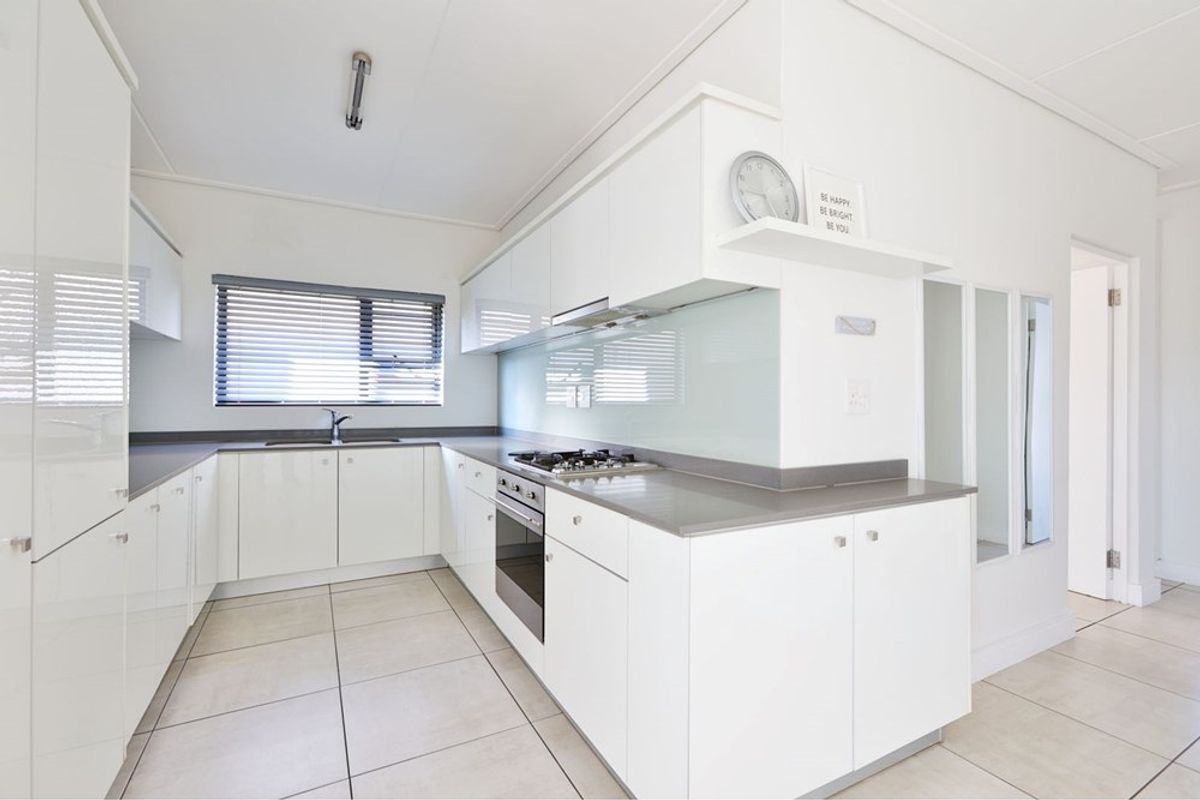 Modern kitchen featuring white gloss cabinetry, stone countertops, a gas hob, integrated oven, and neutral tiled flooring in a clean, minimalist layout.