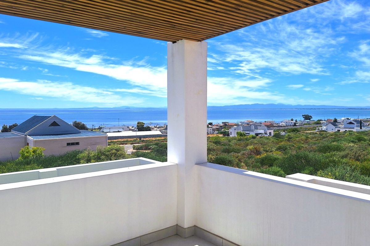 A modern balcony featuring a timber slat ceiling and concrete balustrade, offering expansive coastal and landscape views.