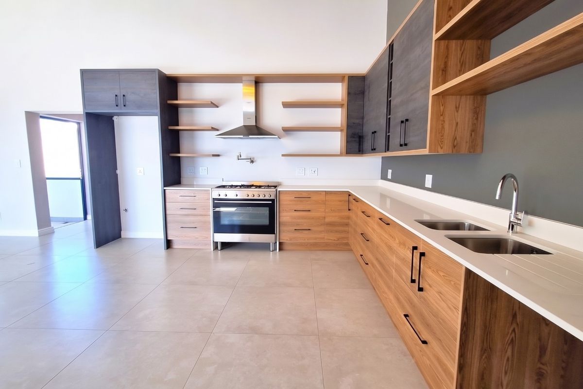 Modern kitchen featuring wood-grain cabinetry, stone countertops, stainless steel gas stove, extractor fan, and double basin sink in an open-plan layout.