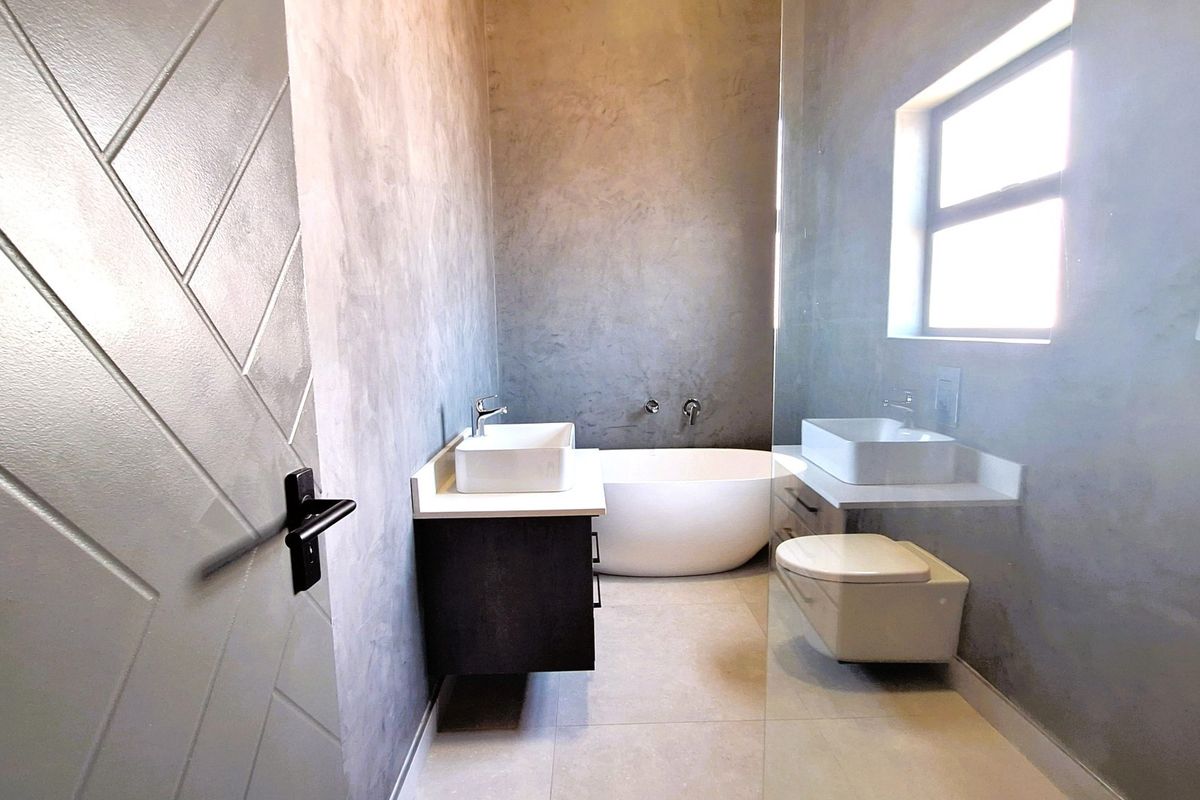 Modern bathroom featuring a freestanding bathtub, dual vessel sinks on floating vanities, wall-mounted toilet, and contemporary cement-style wall finishes.