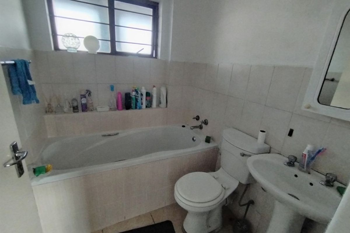 A dated bathroom featuring a built-in bathtub, pedestal sink, and toilet, with tiled walls and a window for natural light.