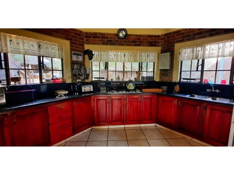 A functional kitchen featuring warm-toned wooden cabinetry, dark countertops, a gas hob, and large windows with views of the garden.