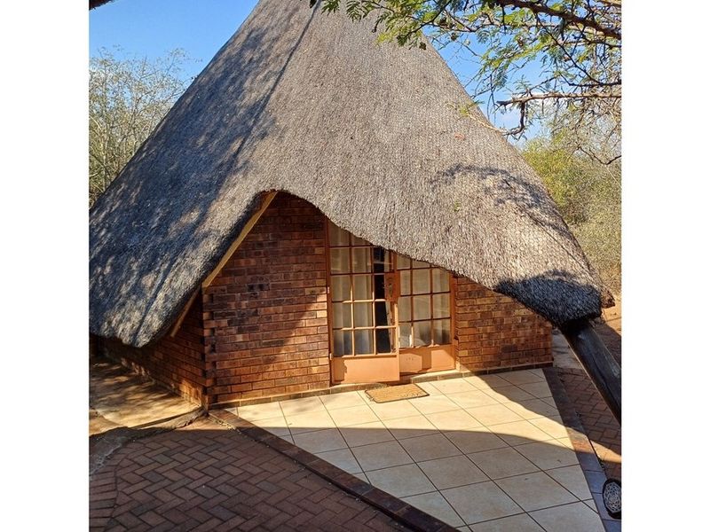 A charming cottage exterior featuring a traditional thatch roof, face brick walls, and a paved entrance patio with french door access.