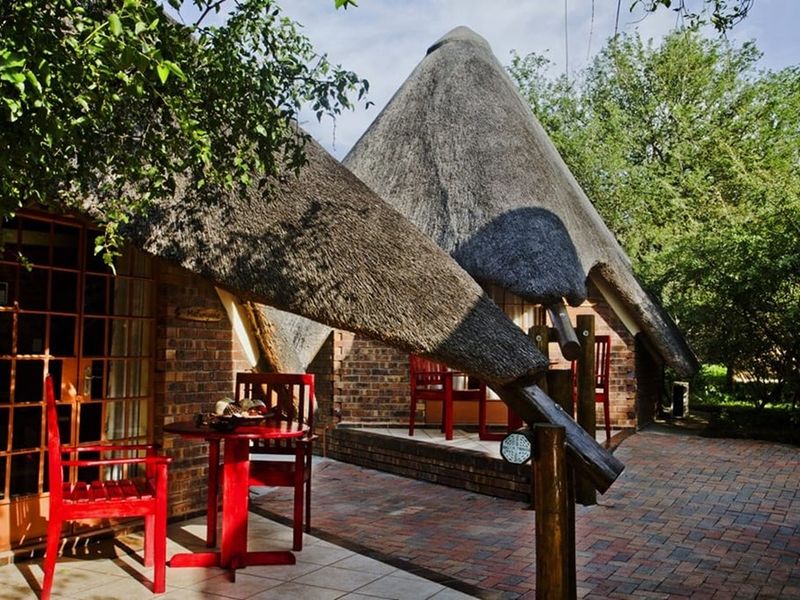 A charming cottage patio area featuring traditional thatched roofing, exposed brickwork, and durable brick paving, offering a cozy outdoor space.