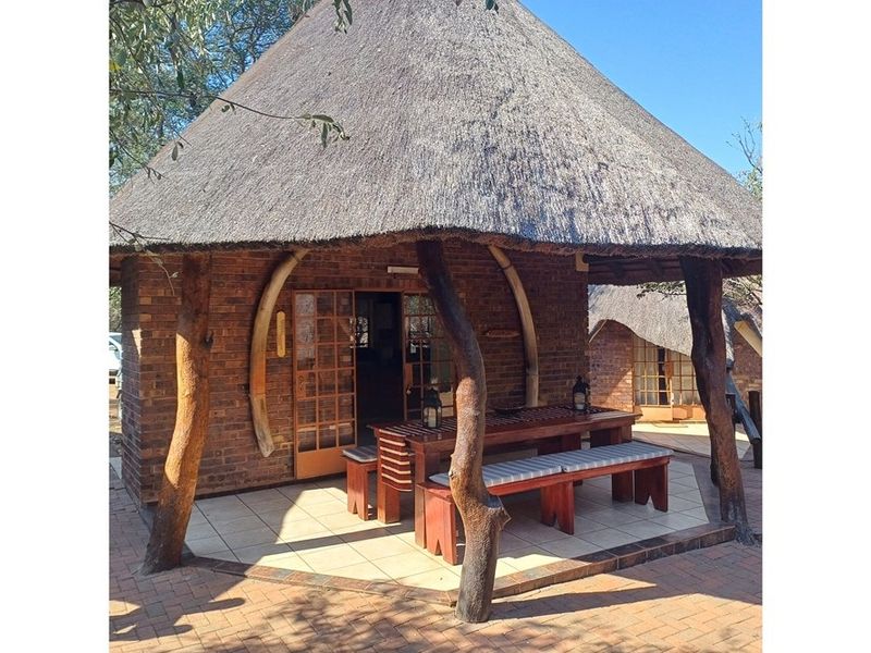 A charming covered patio area featuring a traditional thatched roof, exposed brickwork, and rustic timber support posts, providing a pleasant outdoor seating space.