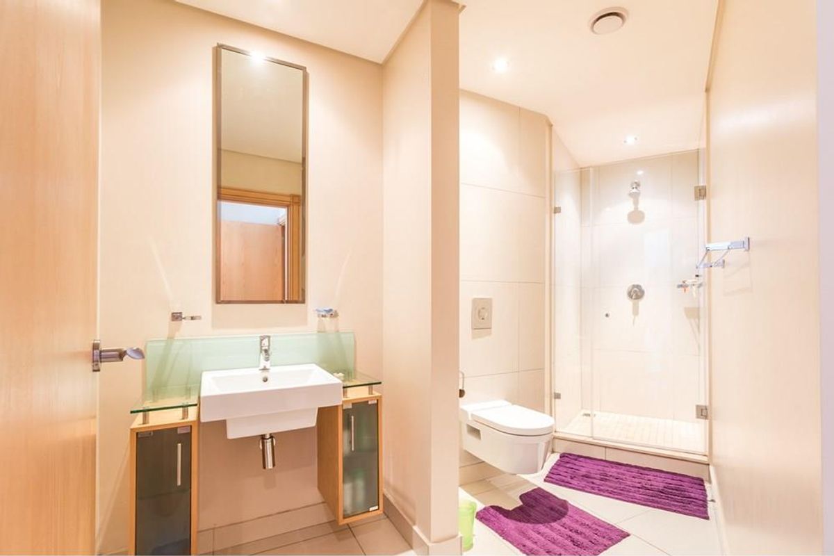 Modern bathroom featuring a wall-mounted vanity with glass shelf, wall-hung toilet, and a glass-enclosed walk-in shower with recessed lighting.