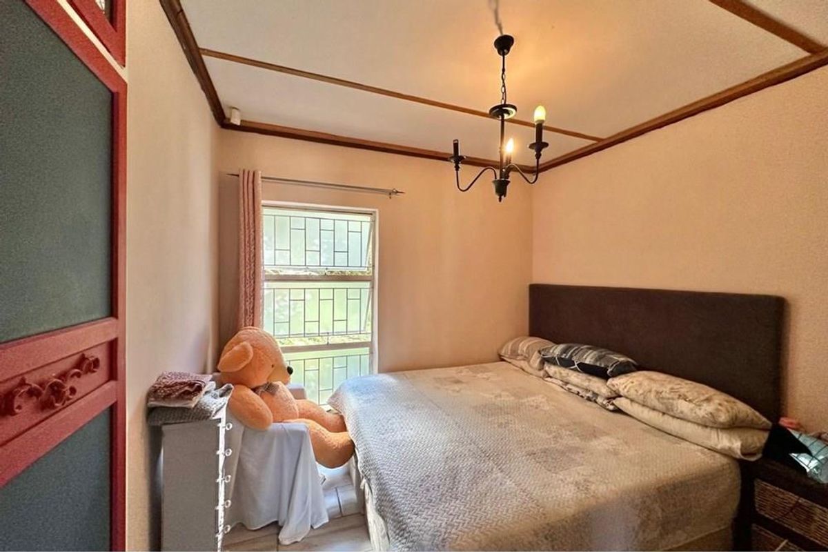 A cozy bedroom featuring a window with security bars, a classic chandelier, and built-in cabinetry.