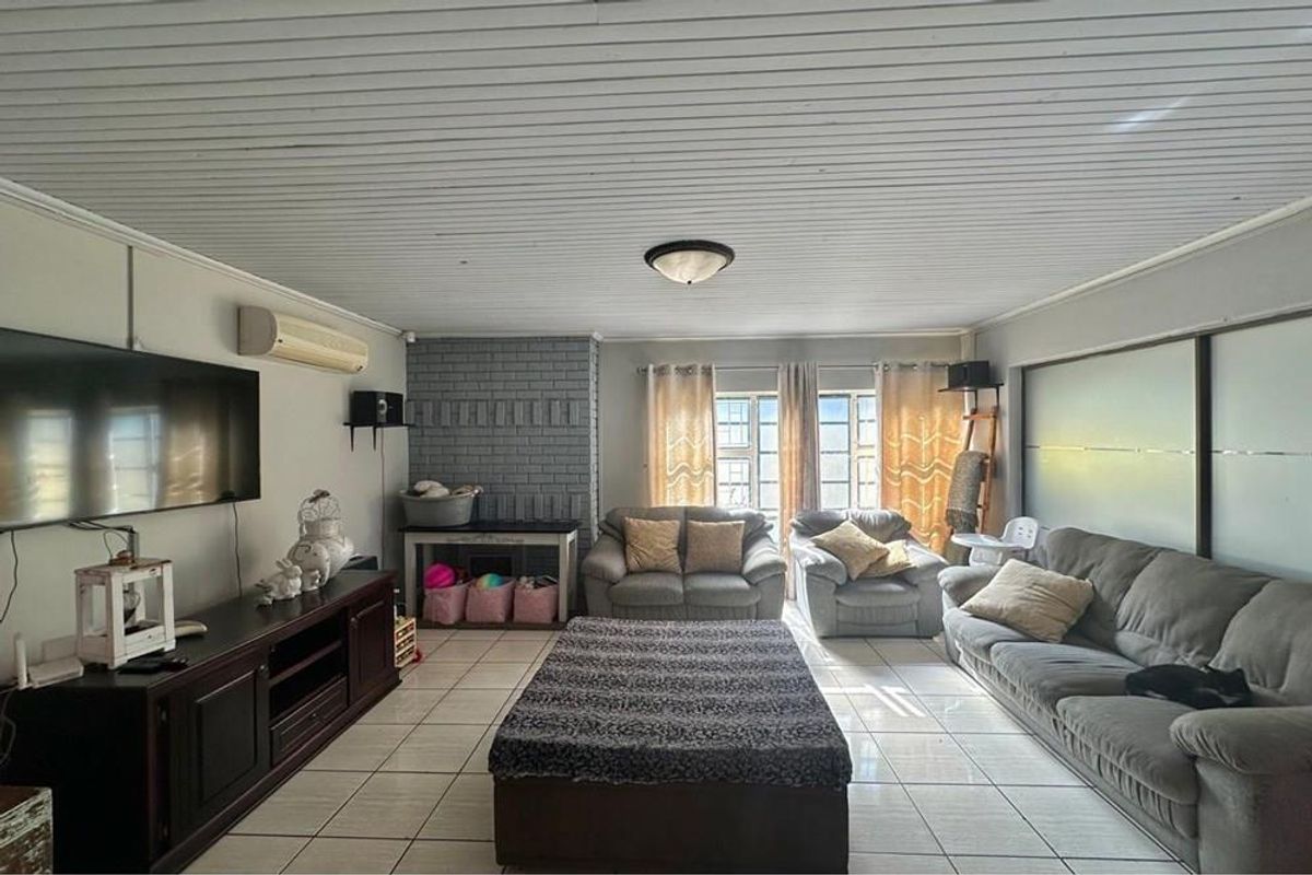 A spacious living room featuring tiled flooring, a painted brick fireplace feature wall, and a white timber-paneled ceiling.