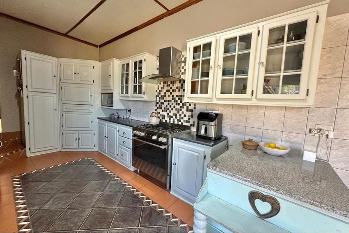 A functional kitchen featuring white cabinetry, a stainless steel gas stove with extractor fan, granite countertops, and tiled flooring.