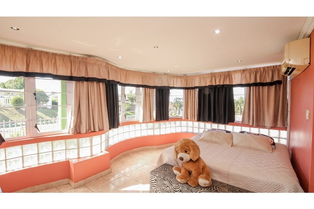 Spacious bedroom featuring a curved wall with glass block accents, tiled flooring, recessed ceiling lighting, and a wall-mounted air conditioning unit.