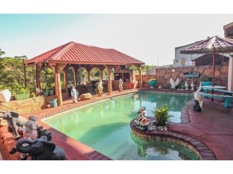 Outdoor pool area featuring a covered patio with a built-in braai, brick paving, and a stone-clad boundary wall.