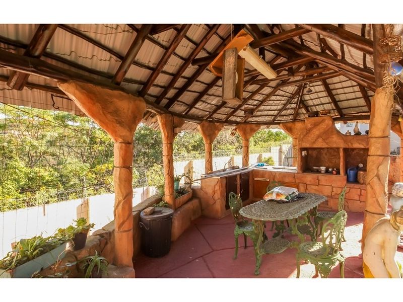 Covered outdoor entertainment area featuring a built-in braai, sink, and rustic stone-clad pillars under a traditional thatched roof.
